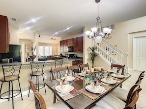 A spacious kitchen with modern appliances, a dining area with a long table set for six, and a staircase leading to another level.