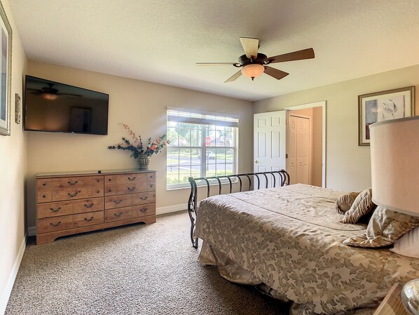 Un dormitorio con cama, cómoda, ventilador de techo, ventana y puerta.