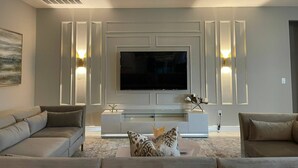 A modern living room with a large flat-screen TV, two sofas, a glass coffee table, and decorative wall sconces. - Last Minute Disney! Private Pool, Hot Tub, Game Room & Themed Bedrooms. Book Now! #60031 (Orlando)