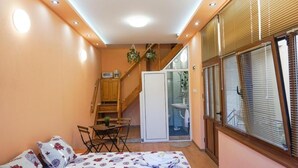 A compact room with a bed, a small table, and a chair. There is a sliding door leading to a bathroom with a sink and a shower. - Pamir Guest House (Troyan)