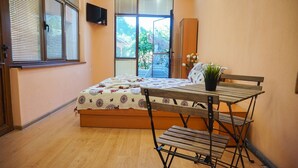A bedroom with a bed, a wooden table with chairs, a potted plant, and a TV on the wall. - Pamir Guest House (Troyan)