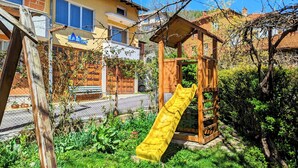 A playground with a yellow slide and a wooden playhouse. - Pamir Guest House (Troyan)