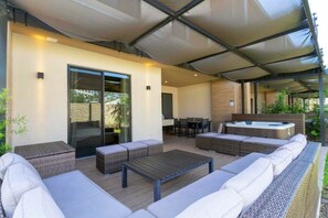 An outdoor patio with wicker furniture, a hot tub, and a covered seating area.