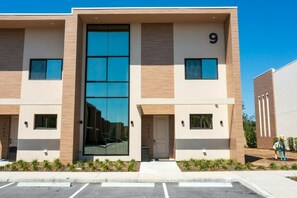 A modern building with a large glass entrance, numbered 9, and a parking lot in front.