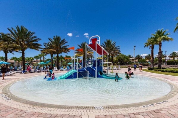 A water play area with slides and a central structure, surrounded by palm trees and lounge chairs.
