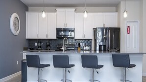Une cuisine moderne avec des meubles blancs, des appareils en acier inoxydable et un coin bar équipé de quatre tabourets.