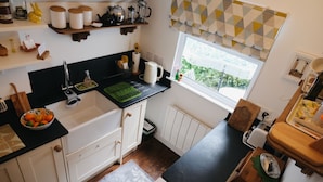 A kitchen with white cabinets, a black countertop, a window with patterned curtains, and a bowl of fruit on the counter. - woodland cottage (barnstaple)