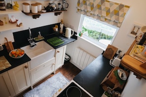 A kitchen with white cabinets, a black countertop, a window with patterned curtains, and a bowl of fruit on the counter.