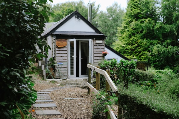 A rustic wooden building with a signboard, a wooden staircase leading to the entrance, and a garden path.