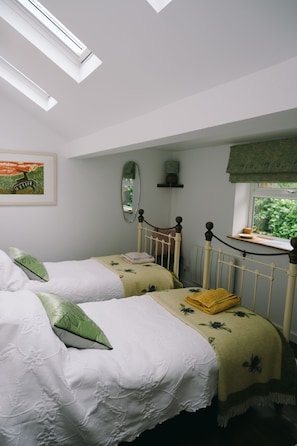 A bedroom with two beds, a window with a view, a radiator, and a mirror on the wall.
