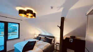 Une chambre avec un grand lit, une fenêtre, un luminaire au plafond et une petite table.