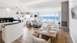 Un espace de vie moderne comprenant une cuisine, un coin repas et un espace détente près d’une grande fenêtre donnant sur la mer.