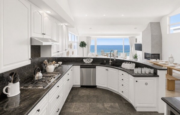 A modern kitchen with white cabinetry, a black countertop, and a view of the ocean.