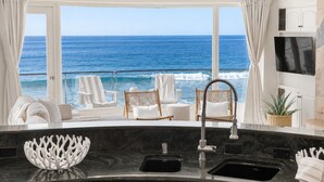 Une cuisine moderne avec vue sur l’océan, comprenant un évier, des chaises blanches et une grande fenêtre.