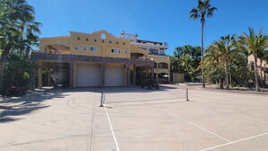 A spacious outdoor area with a tennis court, palm trees, and a building with multiple garages.