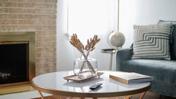 Un salon avec une cheminée, une table basse ronde sur laquelle se trouvent un livre et un vase rempli de plantes séchées, et un canapé agrémenté de coussins à motifs.