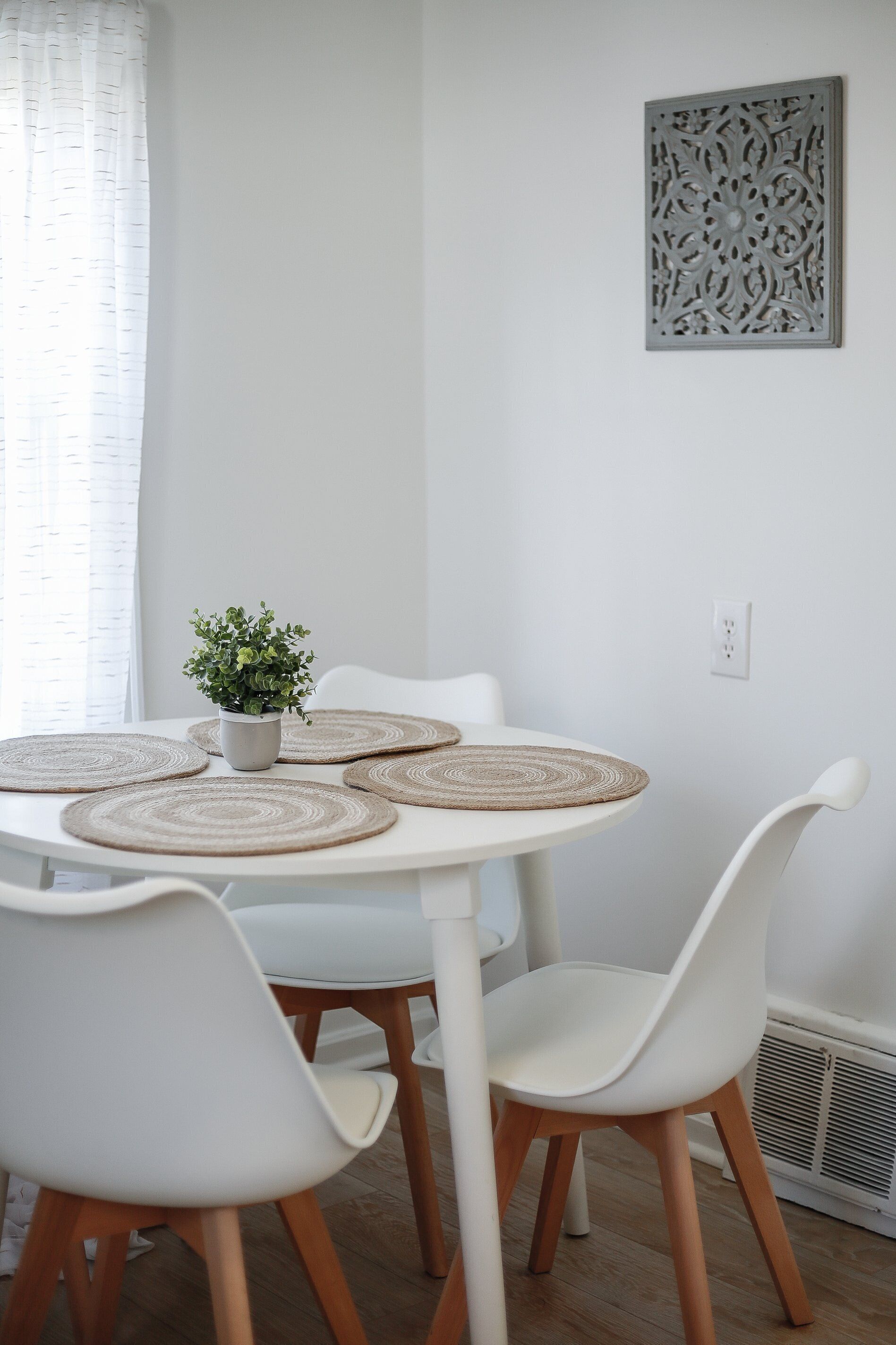 Une table à manger blanche avec quatre chaises, une petite plante en pot et un élément décoratif mural.