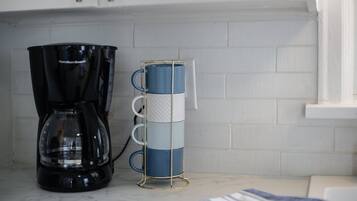 A kitchen with a black coffee maker and a stack of blue and white mugs on a white countertop.