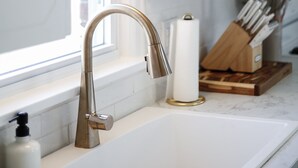 Une cuisine moderne avec un robinet en acier inoxydable, un luminaire suspendu en bois et un bloc à couteaux posé sur le plan de travail.