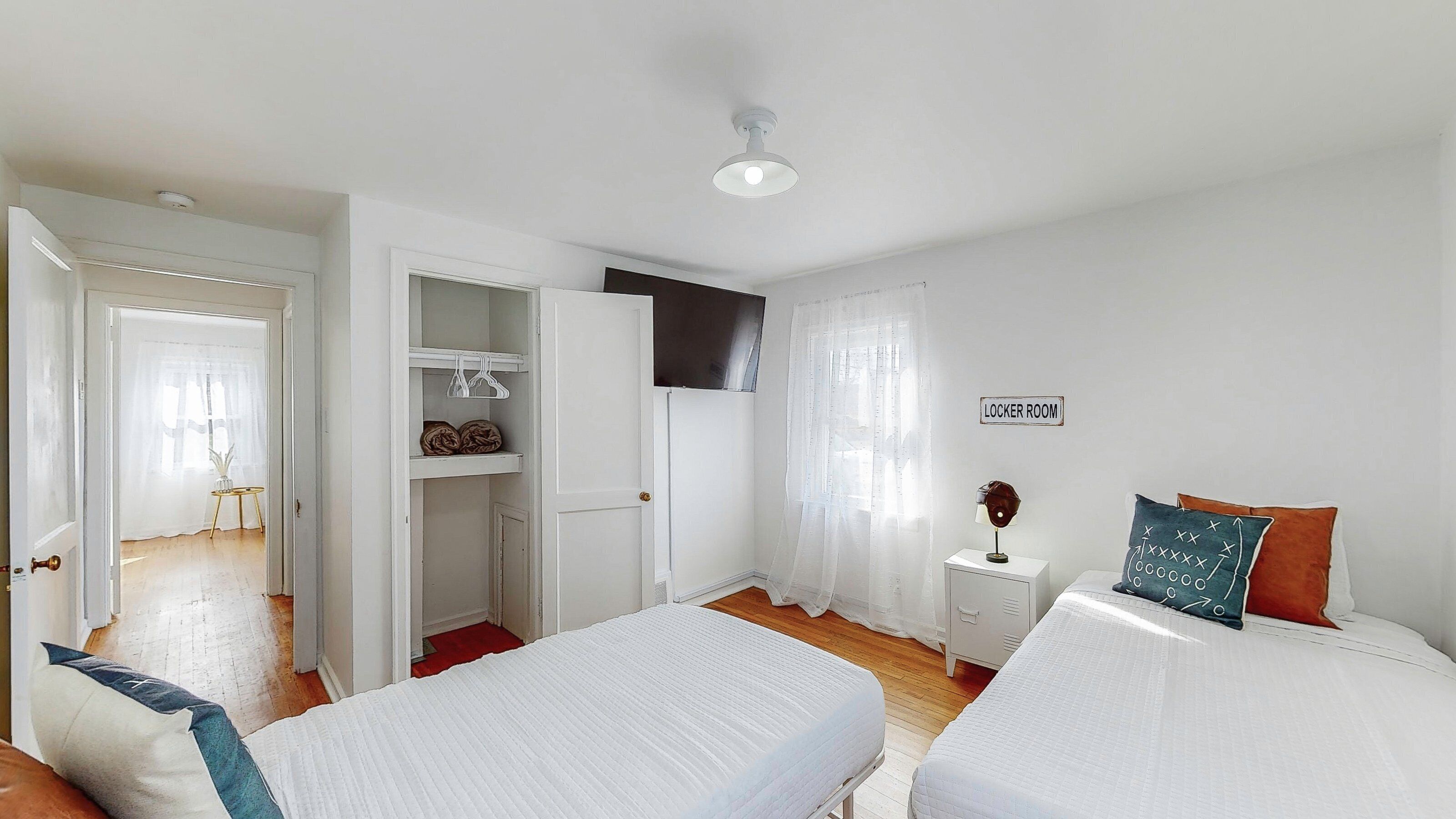 A room with two beds, a wardrobe, a small table with a lamp, and a sign indicating a locker room.