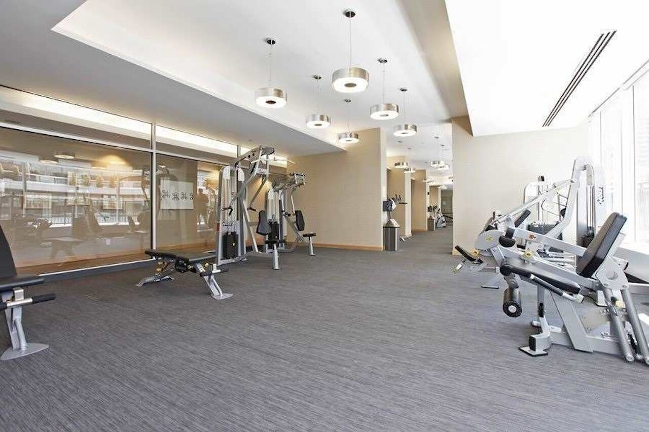 A modern gym with various exercise machines, large windows, and a clean, spacious layout.