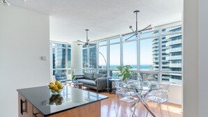 A modern living room with a glass dining table, a sofa, and a view of the ocean. - Maple Leaf Square Executive Suite (Toronto)
