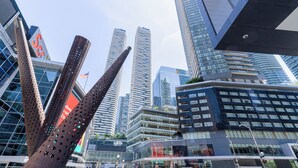 Ein modernes Stadtbild mit Hochhäusern, einer markanten Skulptur und wolkenlosem Himmel.