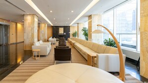 Eine moderne Hotelhalle mit einer langen Couch, einem runden Tisch und einem Empfangsbereich im Hintergrund.