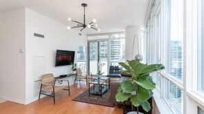 A modern living room with a flat-screen TV, wicker chairs, a coffee table, and a large plant. - Maple Leaf Square Executive Suite (Toronto)