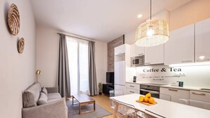 Eine moderne Küche mit einem 'Coffee & Tea' Schild, ein Essbereich mit Tisch und Stühlen sowie ein Wohnzimmer mit Sofa und Couchtisch.