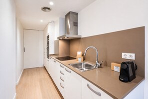 Una cocina moderna con un lavamanos de acero inoxidable, horno empotrado y campana extractora. Hay armarios con tiradores plateados y una encimera con una cafetera y una caja con la etiqueta 'Sweet Inn'.