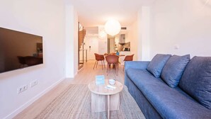 A modern living room with a flat-screen TV, a blue sofa, and a dining area with chairs and a table. - Sweett | Girona B1 - Two Bedroom Apartment, Sleeps 5 (Barcelona)