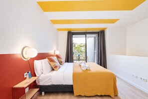 Una habitación de hotel con cama, mesita de noche, lámpara, ventana con cortinas y vistas al exterior.