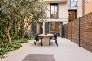 Une terrasse extérieure moderne, dotée d’une table et de chaises, entourée de verdure et d’une clôture en bois.