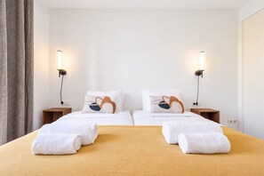 A hotel room with two beds, each with a unique pillow design, bedside lamps, and neatly folded towels on the bed. - Sweett | Girona B2 - Four Bedroom Apartment, Sleeps 10 (Barcelona)