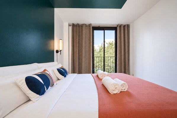 Habitación de hotel con cama, mesita de noche, ventana con cortinas y vista a follaje exterior.