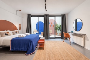 A modern hotel room with a large bed, a desk, and a view of the cityscape.
