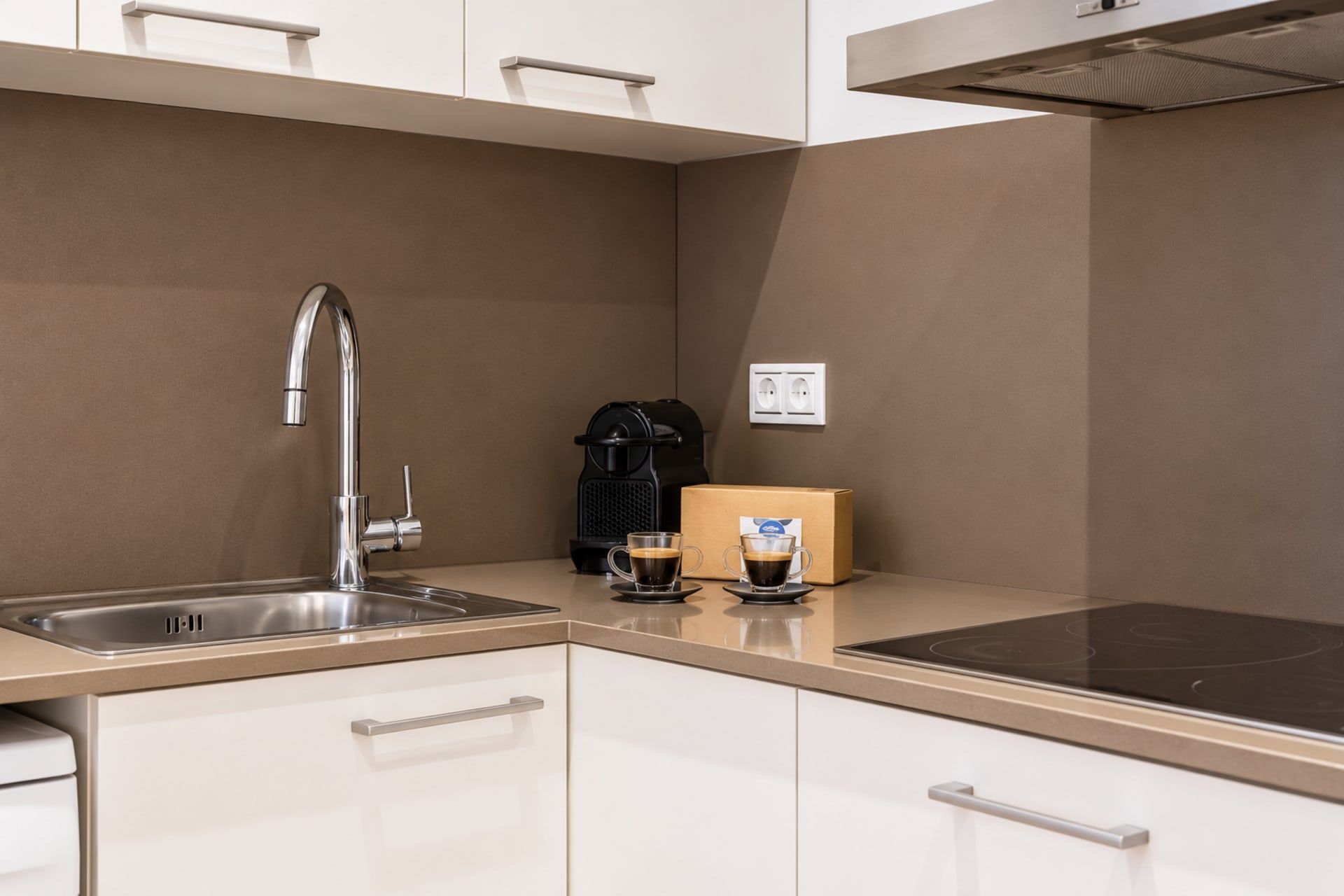 Una cocina moderna con un lavamanos de acero inoxidable, una cafetera y una caja de cápsulas de café.