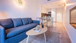 Un salon moderne avec un canapé gris, une table basse ronde et un coin cuisine à l’arrière-plan.