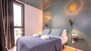 Un dormitorio moderno con una cama grande, dos apliques de pared, una mesita de noche y un ventanal con cortinas.