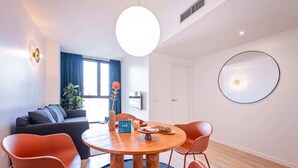 Una sala de estar moderna con una mesa de comedor redonda de madera, sillas anaranjadas, un sofá y un espejo grande en la pared.