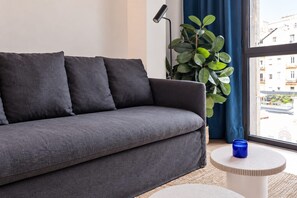 A grey sofa with cushions, a floor lamp, a potted plant, and a small round table with a blue candle.