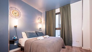 Ein Schlafzimmer mit einem Bett, zwei Wandleuchten, einem Fenster mit Vorhängen und einer Wasserflasche auf einem Nachttisch.