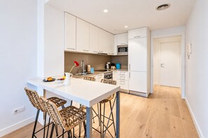 A modern kitchen with white cabinetry, a central island with bar stools, and a microwave.
