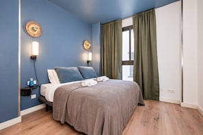 Une chambre à coucher avec un lit, deux lampes fixées au mur, une fenêtre avec des rideaux et un plancher en bois.