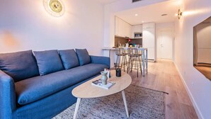 Ein modernes Wohnzimmer mit einem grauen Sofa, einem runden Couchtisch und einer dahinterliegenden Küchenzeile.