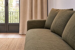 Een groene bank met een geweven vloerkleed, een schuifdeur en uitzicht op groen buiten.