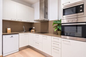 Een moderne keuken met witte kasten, roestvrijstalen apparatuur en een potplant.