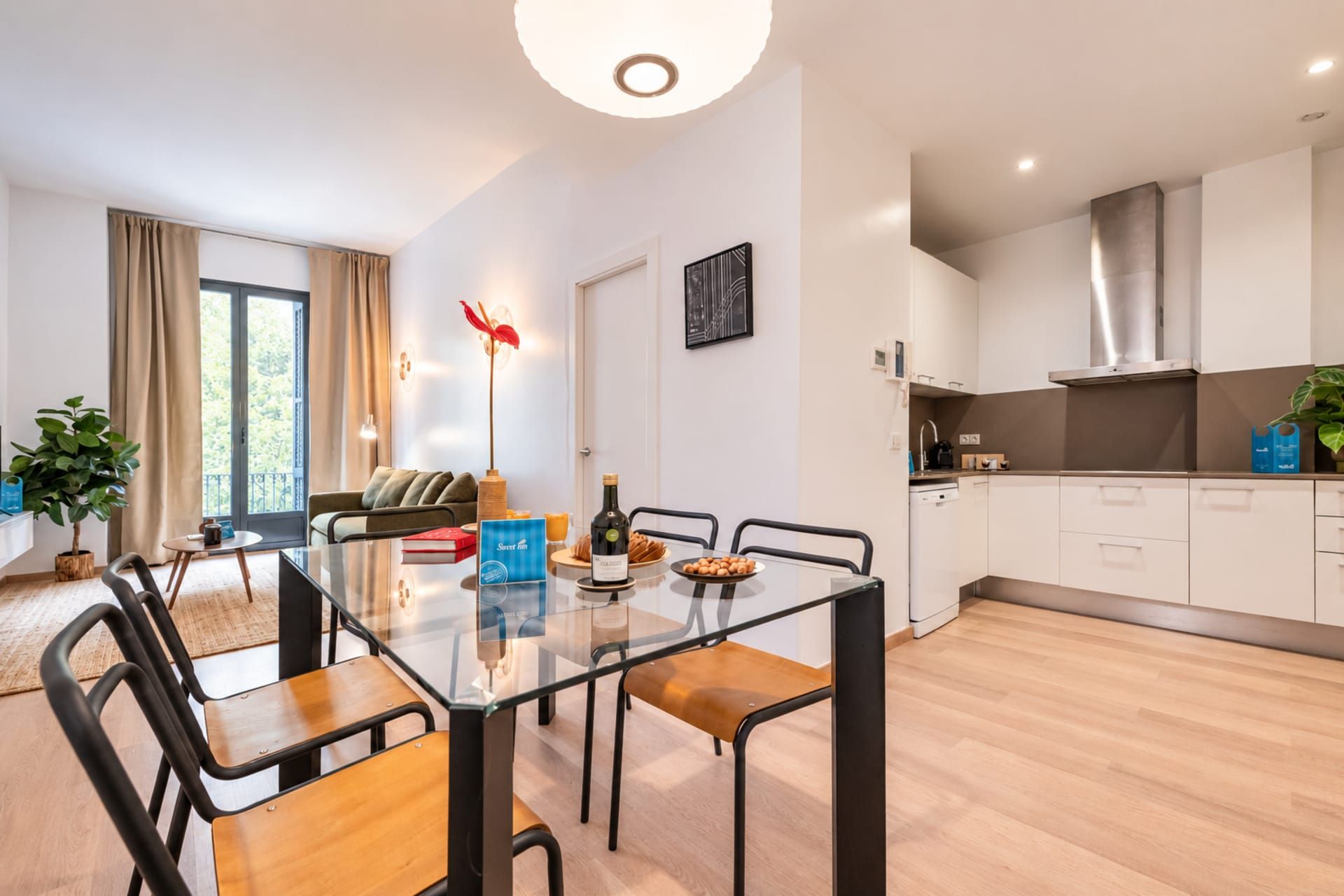 Una cocina moderna con gabinetes blancos, una campana de acero inoxidable y un comedor con mesa y sillas de vidrio.