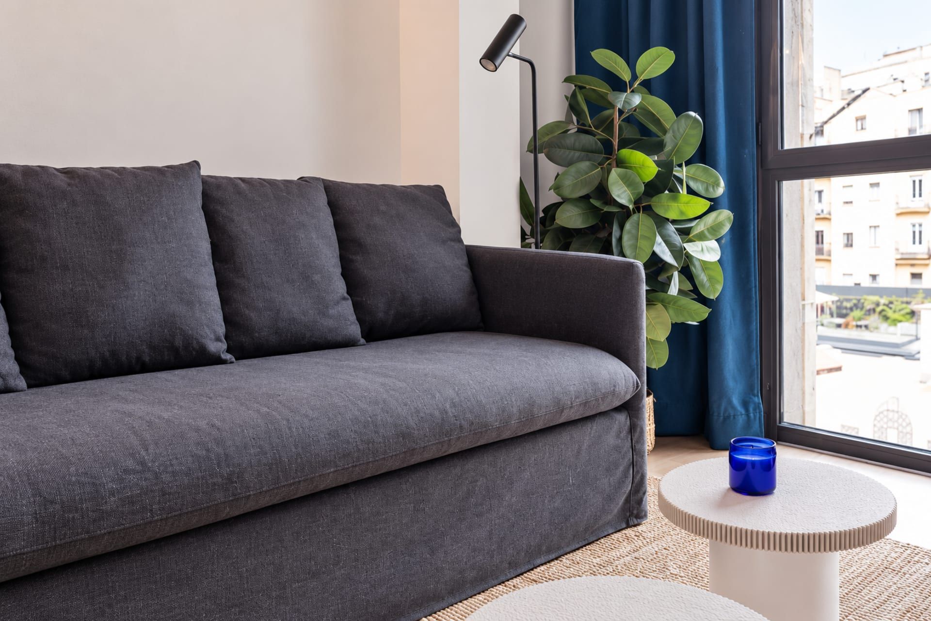 A grey sofa with cushions, a floor lamp, a potted plant, and a small round table with a blue candle.